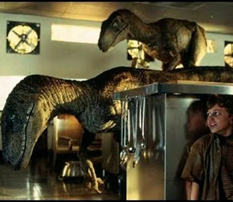 Dos velociraptors en una cocina mientras Tim Murphy se esconde de ellos