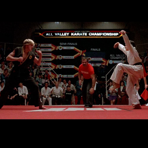 Imagen de daniel larusso a punto de realizar su movimiento icónico la patada de la grulla en la película the karate kid.